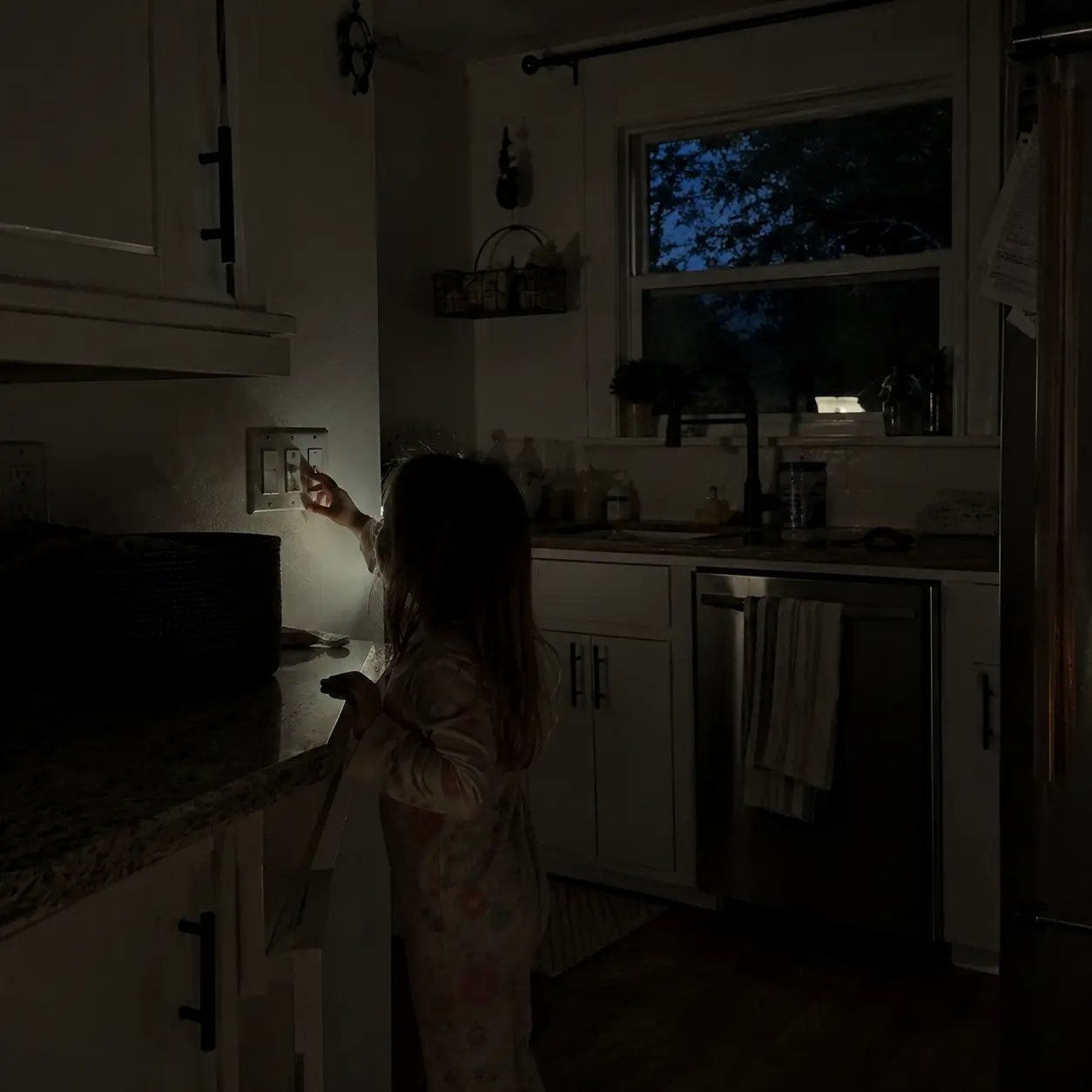 A little girl reaching for a light switch in a dark kitchen after the power was cut